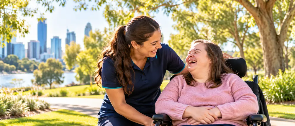 A support worker and a laughing woman in a wheelchair in a sunny park